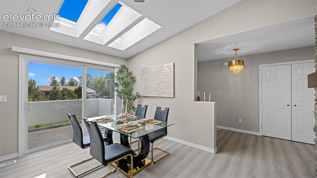 Image 11 of 48: Dining area featuring a vaulted ceiling with four skylights, light wood-fin