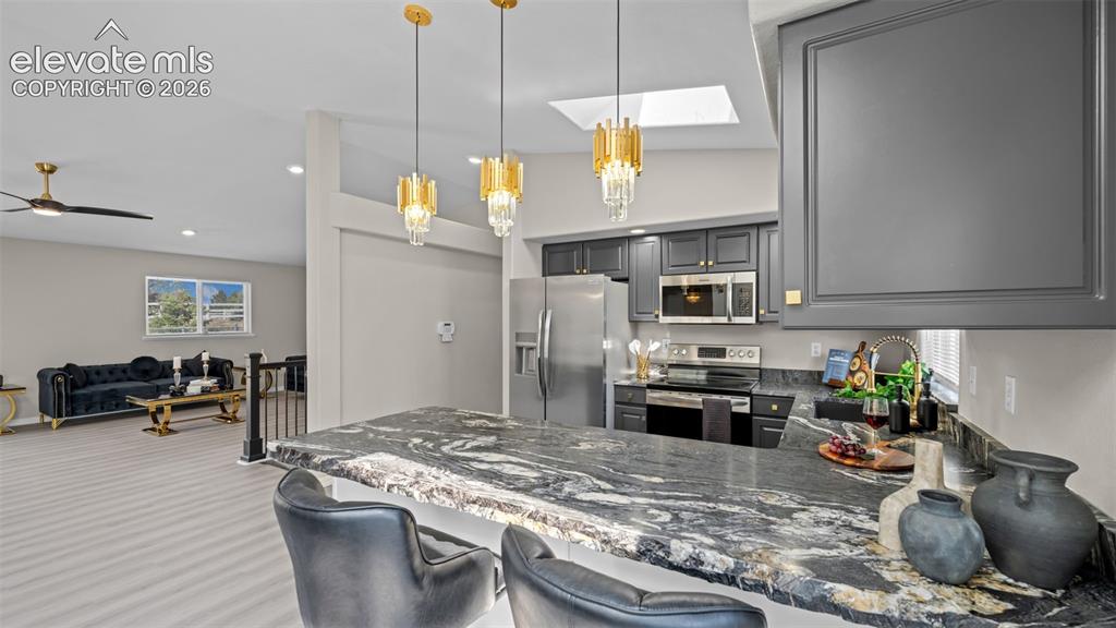 Image 17 of 48: Kitchen island with a dark granite countertop, gold-toned pendant lighting,