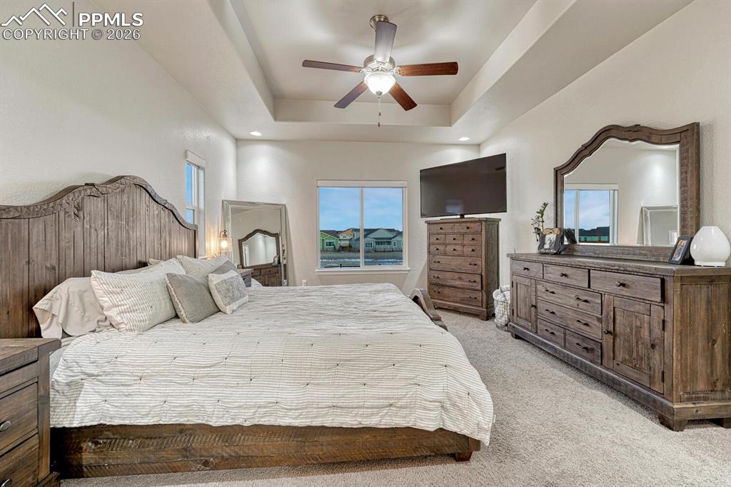 Image 24 of 46: Bedroom featuring light carpet, a tray ceiling, and ceiling fan