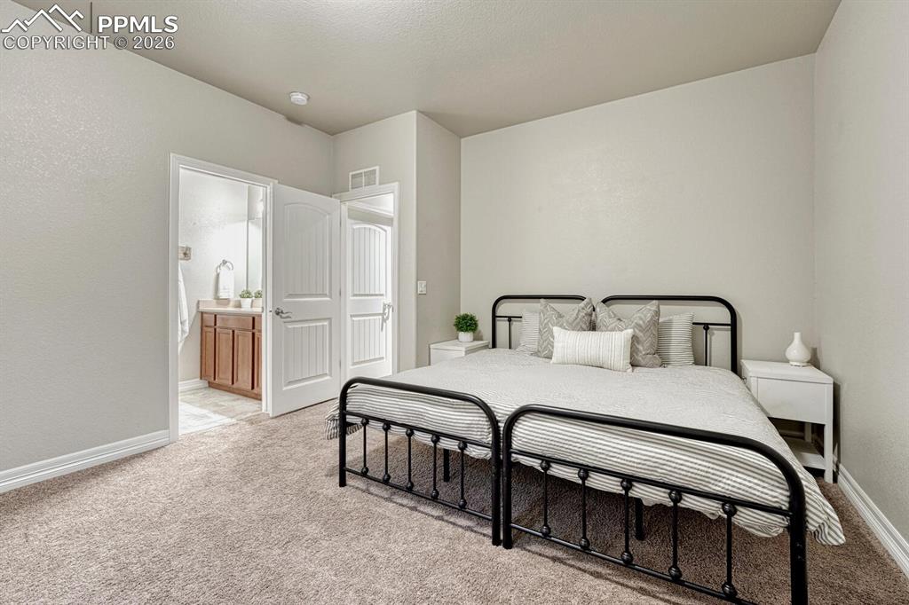 Image 34 of 46: Bedroom with light carpet, a textured wall, and ensuite bathroom