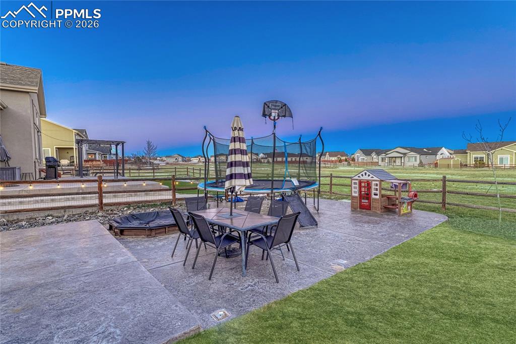Image 38 of 46: Fenced backyard with a trampoline, outdoor dining space, a patio, a residen