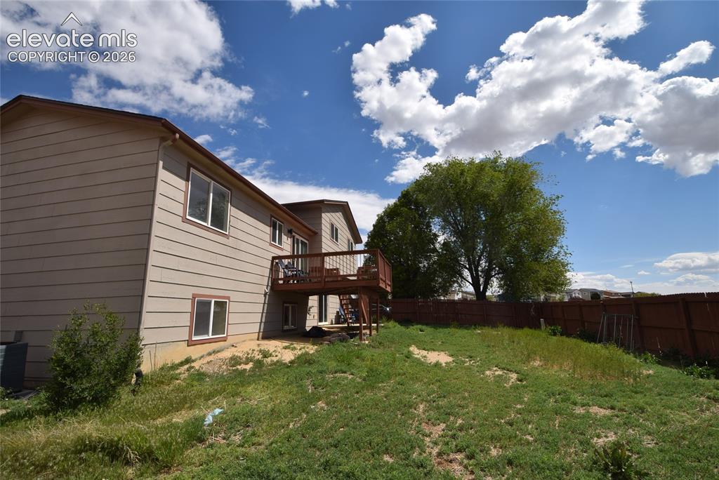 Image 42 of 45: Rear exterior featuring a spacious wood deck, tan siding, and a fenced back