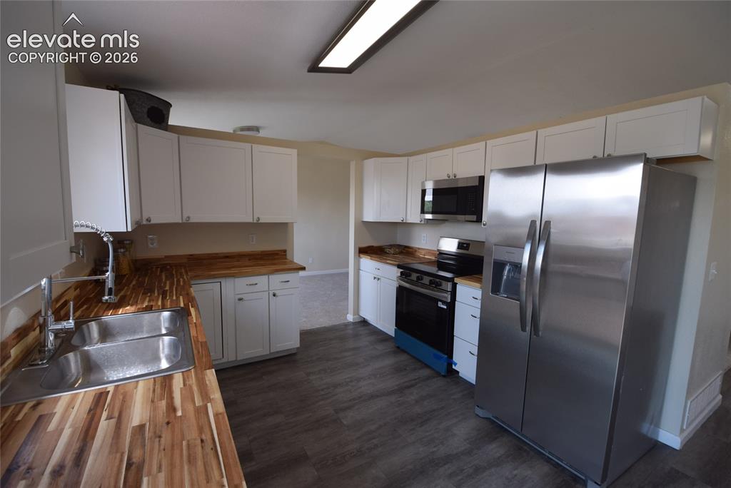 Image 7 of 45: Kitchen featuring extensive butcher block countertops, white cabinetry, sta