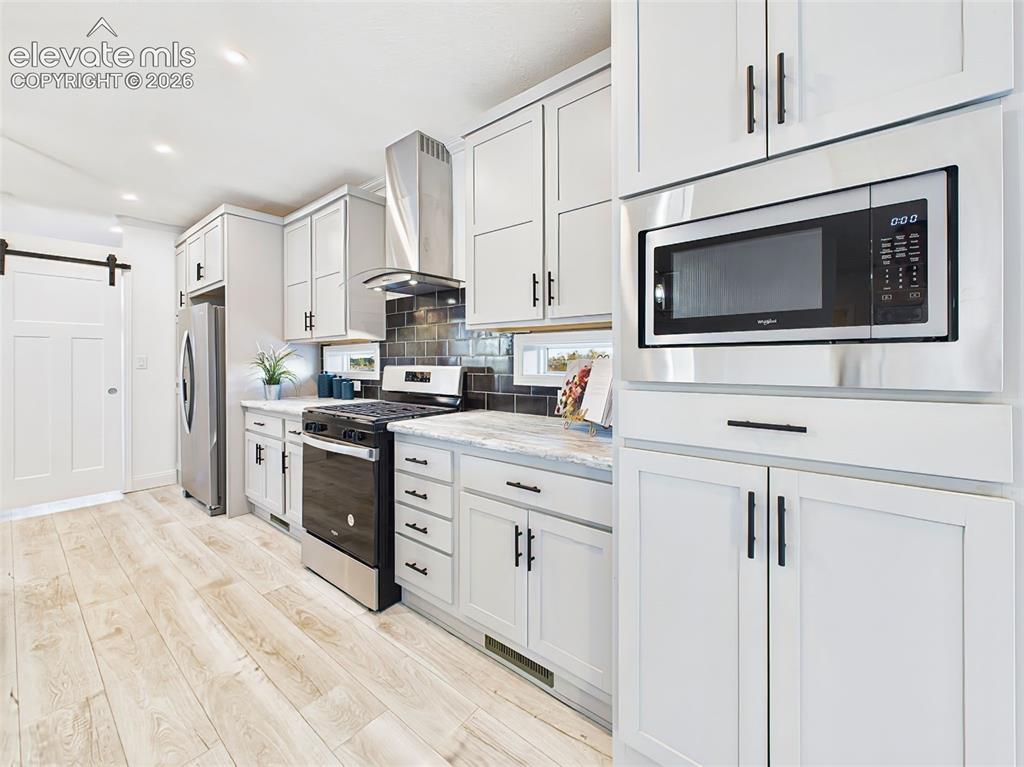 Image 14 of 50: Stylish combination of light gray cabinetry, tile backsplash, and barn door