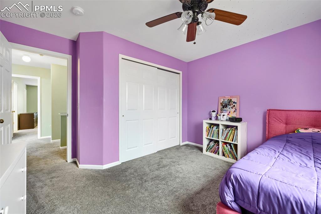 Image 25 of 32: Carpeted room with a ceiling fan, white bi-fold closet doors, and light pur