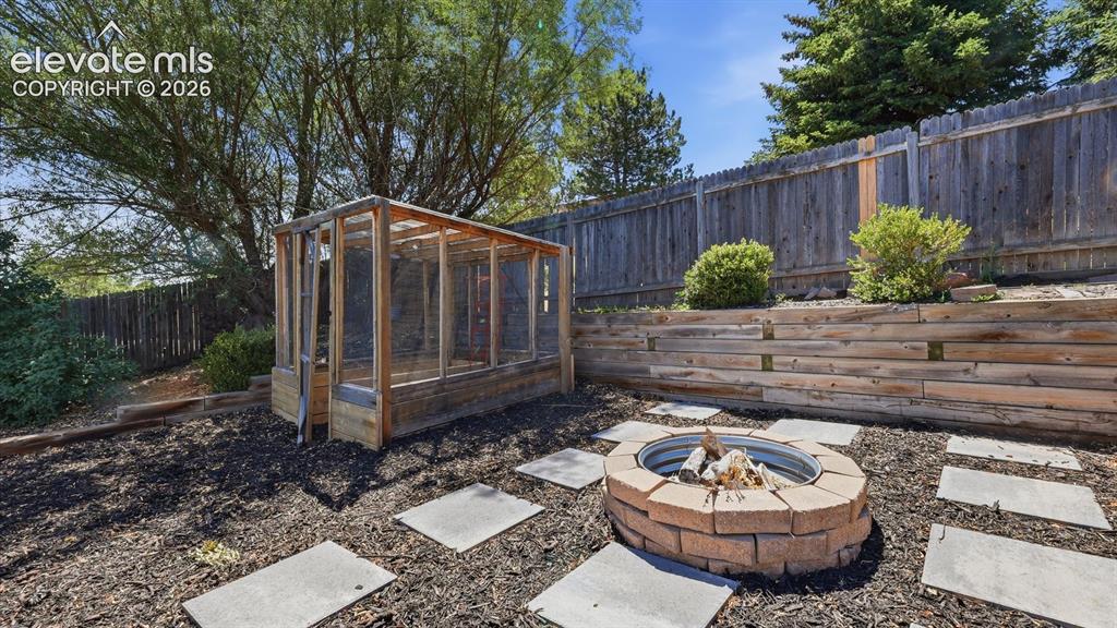 Image 44 of 50: The fenced backyard has terraced beds, a greenhouse for growing flowers or