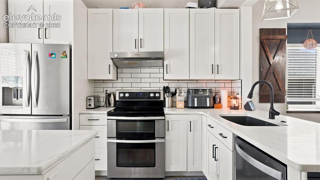 Image 7 of 50: Island kitchen complete with white cabinetry, quartz countertops, subway ti