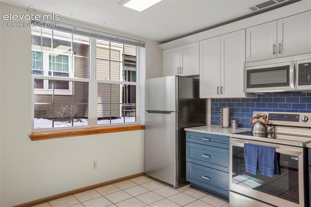 Image 10 of 50: Kitchen with white cabinetry, light tile patterned floors, stainless steel