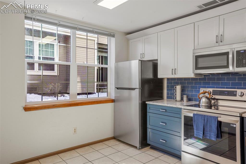 Image 11 of 50: Kitchen with white cabinetry, light tile patterned floors, stainless steel 
