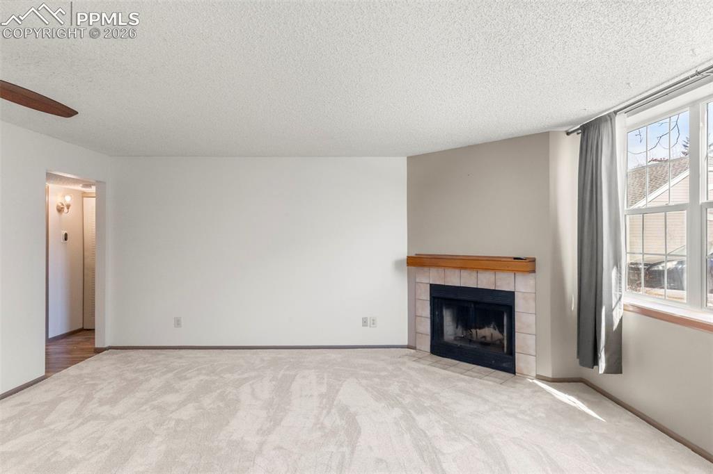 Image 38 of 50: Unfurnished living room with a fireplace, light carpet, ceiling fan, and a