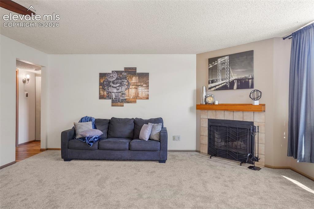 Image 4 of 50: Carpeted living room with a tiled fireplace, a textured ceiling, and ceilin