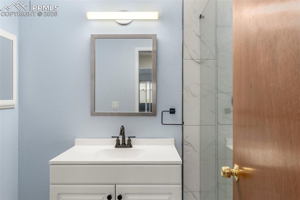 Image 44 of 50: Full bathroom featuring vanity, a marble finish shower, and a textured wall