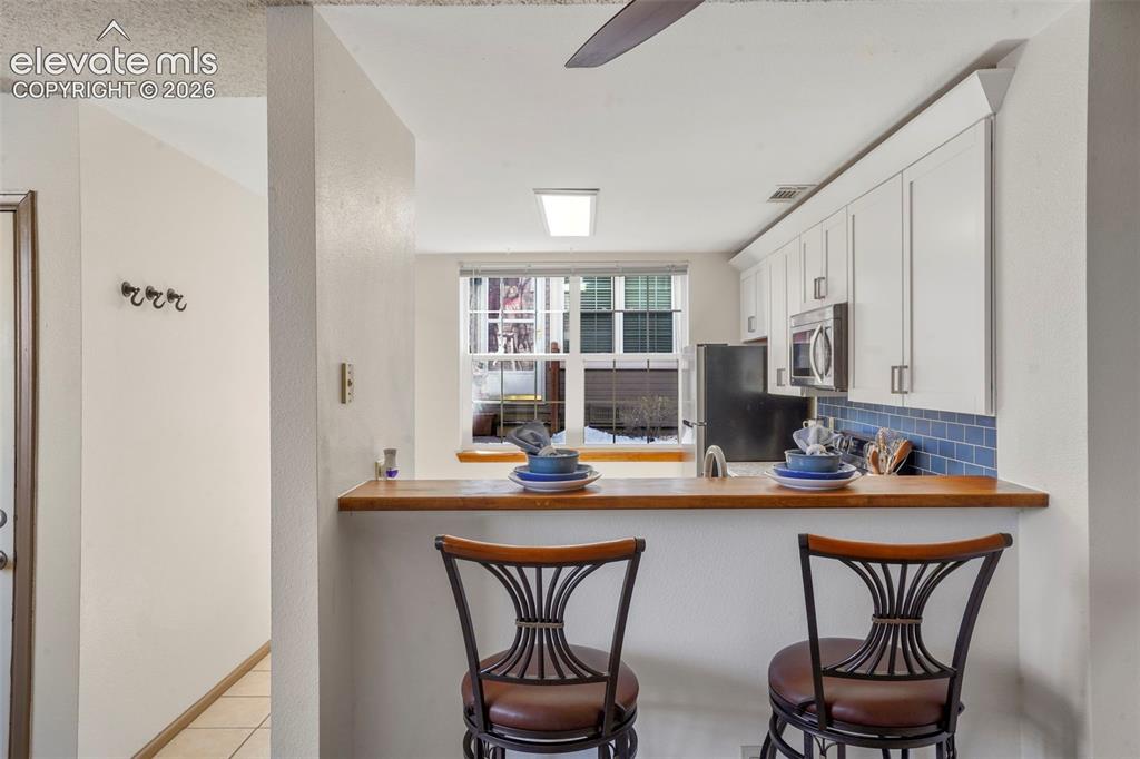 Image 6 of 50: Kitchen with white cabinetry, a kitchen bar, backsplash, appliances with st
