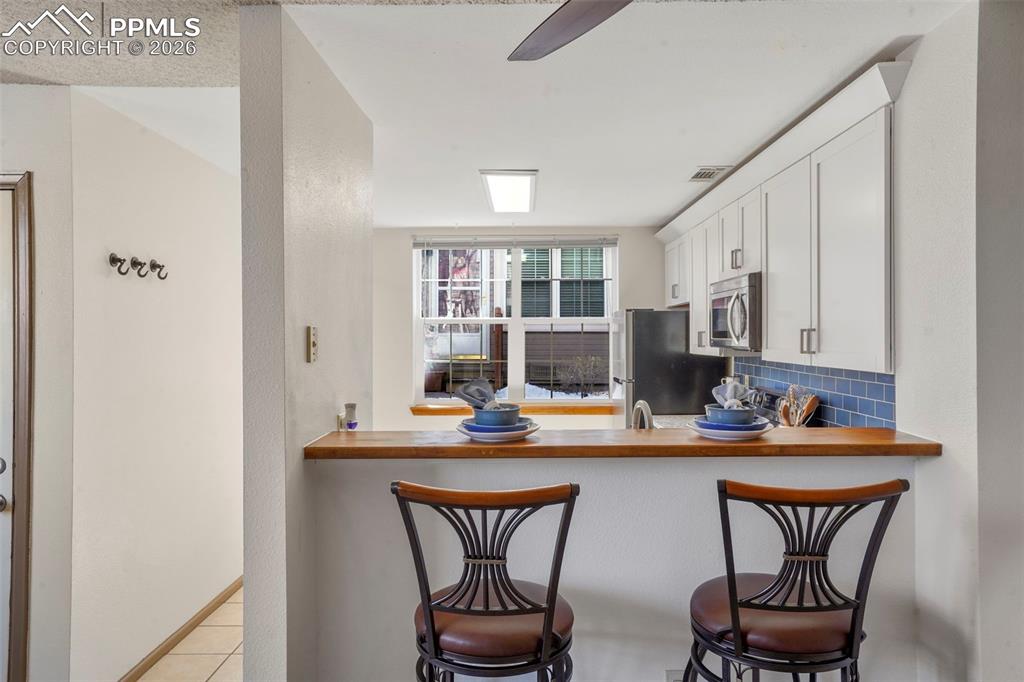 Image 7 of 50: Kitchen with white cabinetry, a kitchen bar, backsplash, appliances with st