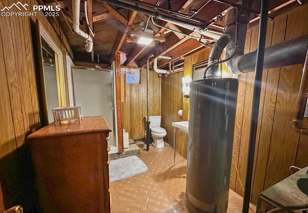 Image 15 of 19: Bathroom with wooden walls, light floors, water heater, a shower stall, and