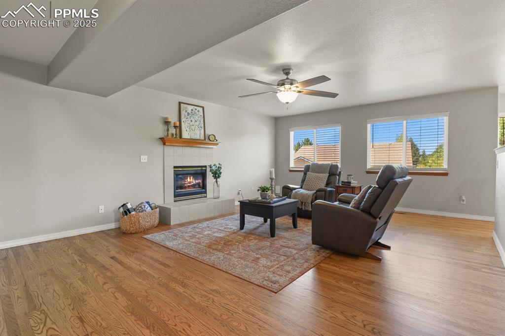 Image 16 of 50: Living area with a tile fireplace, wood finished floors, and a ceiling fan