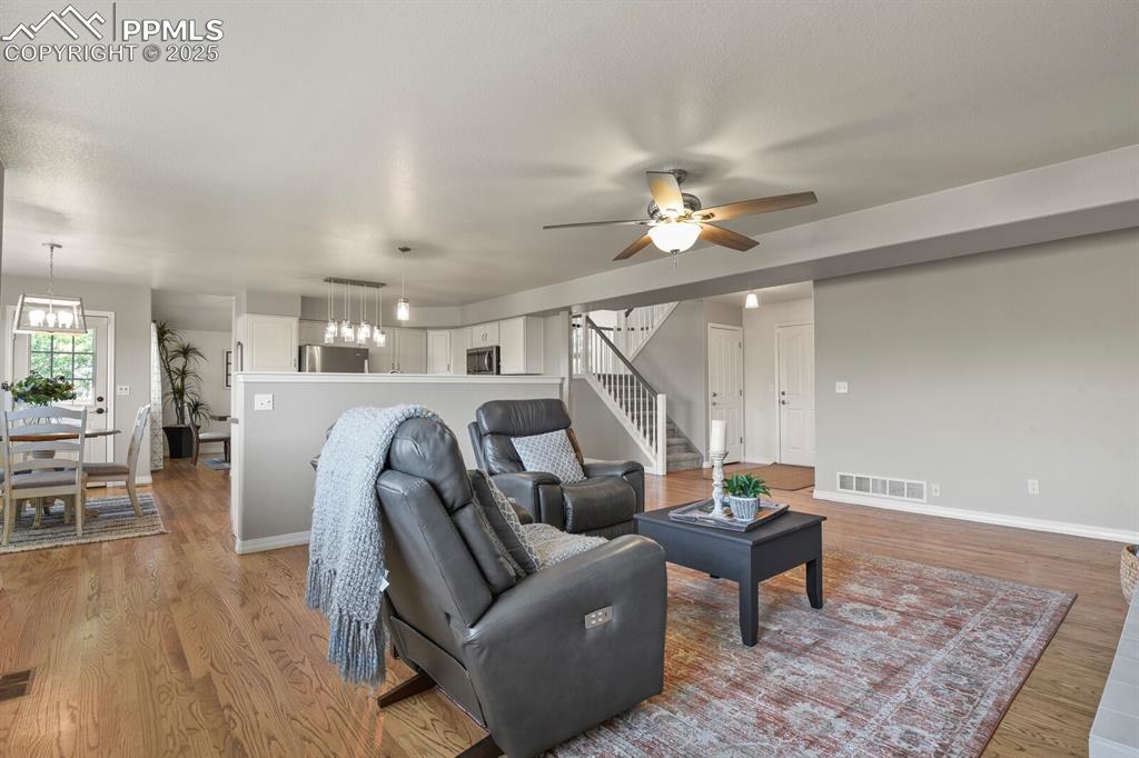Image 18 of 50: Living room with ceiling fan, stairs, and light wood-style flooring