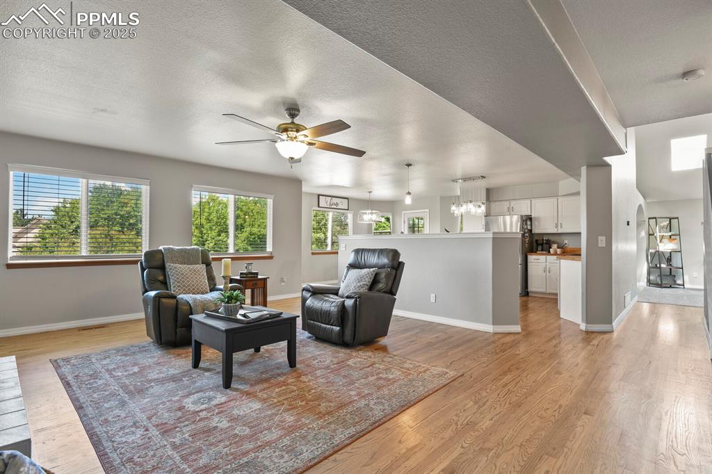 Image 19 of 50: Living room featuring light wood-style flooring, ceiling fan, a textured ce