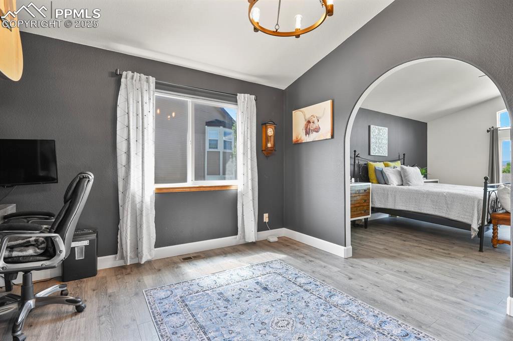 Image 25 of 50: Bedroom with lofted ceiling, wood finished floors, a chandelier, arched wal
