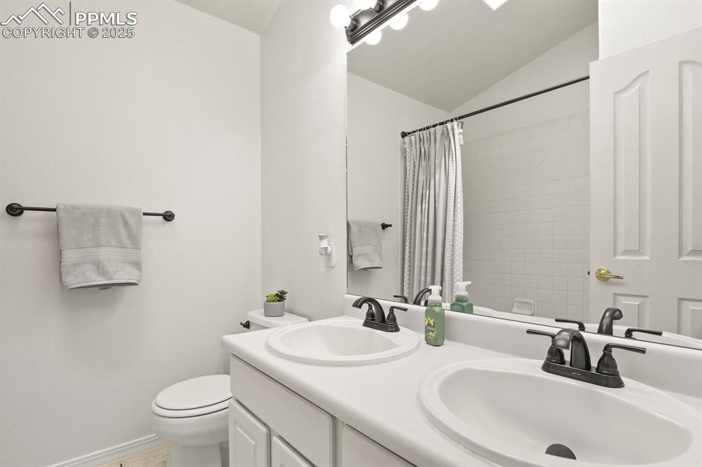 Image 28 of 50: Bathroom featuring vaulted ceiling, double vanity, and a shower with curtai