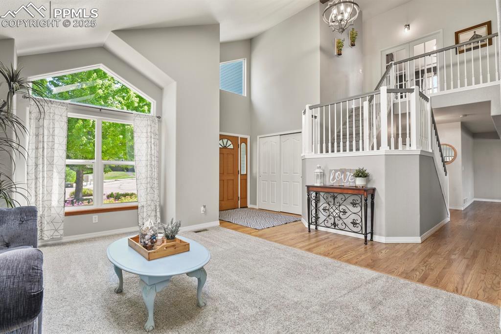 Image 5 of 50: Living area with stairway, a high ceiling, a chandelier, and wood finished 