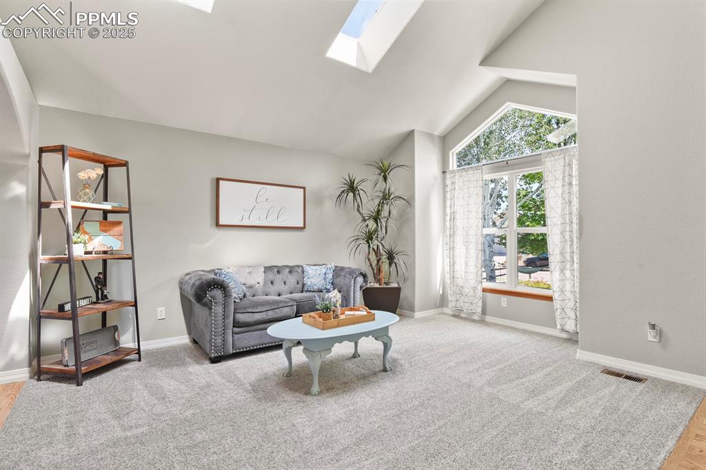 Image 7 of 50: Living area with a skylight, wood finished floors, and high vaulted ceiling