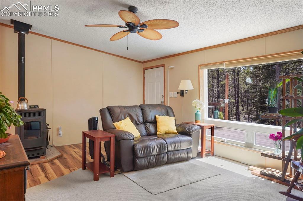 Image 4 of 29: Living area with crown molding, a textured ceiling, a wood stove, wood fini
