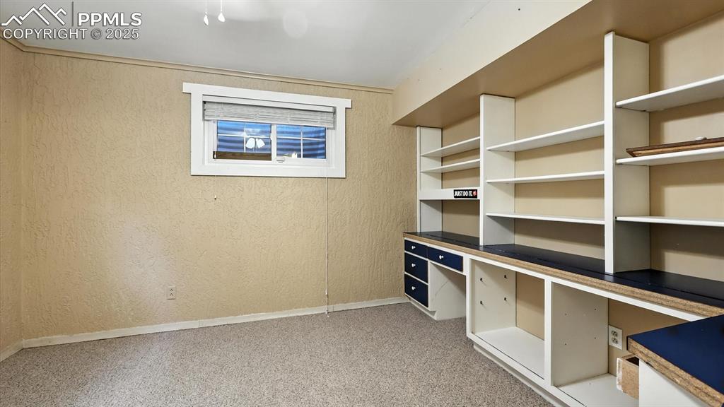 Image 43 of 50: Basement Bedroom #5/Home Office with built-in desk, shelves, and generous c
