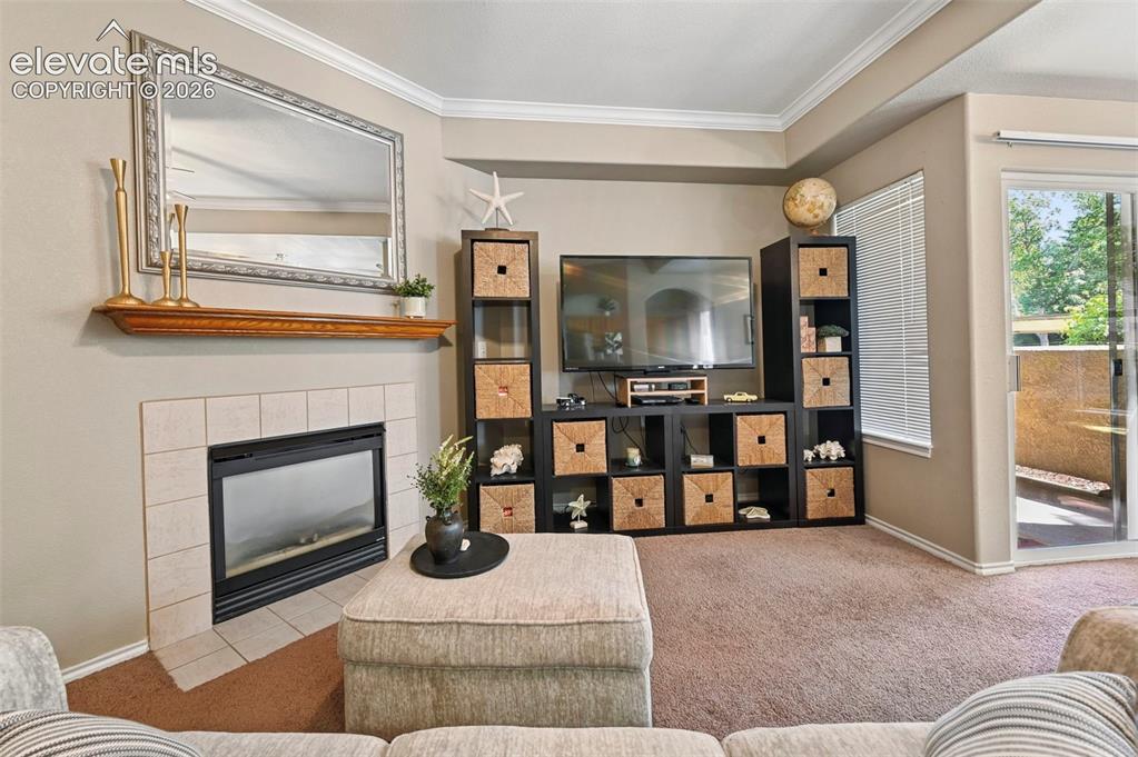 Image 12 of 36: Living area featuring a tiled fireplace with a wood mantle, crown molding,