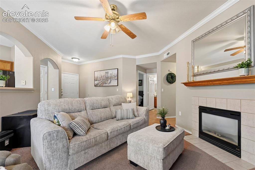 Image 16 of 36: Living room featuring a ceiling fan, crown molding, arched doorways, a fire