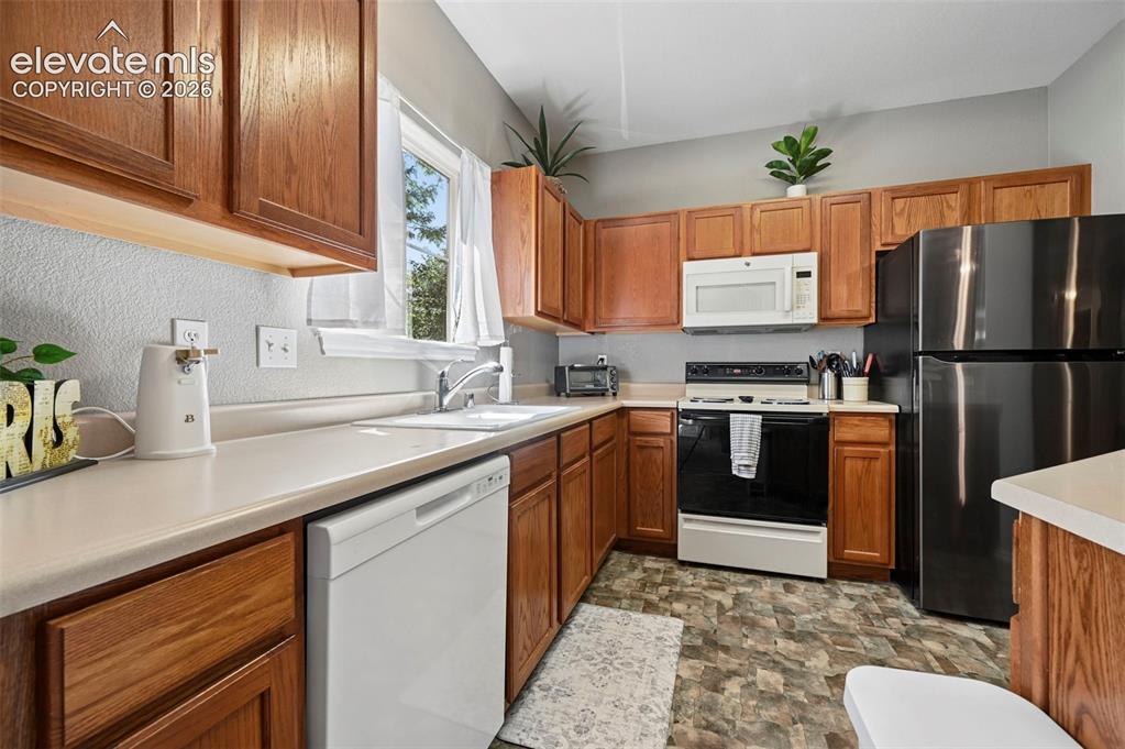 Image 20 of 36: Kitchen featuring warm wood cabinetry, light-toned countertops, window with