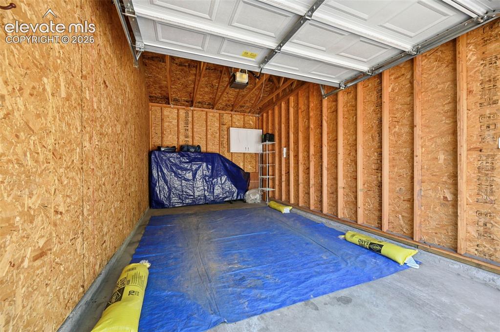 Image 35 of 36: Spacious garage featuring a concrete floor, exposed wood framing, and an ov