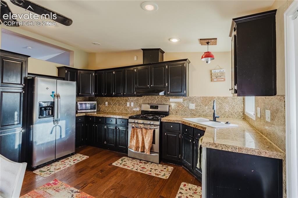 Image 12 of 30: Kitchen featuring dark wood cabinetry, granite-style countertops, stainless