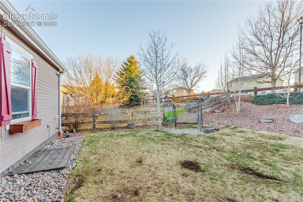 Image 29 of 30: Expansive backyard featuring a sloped landscape with a wood fence, mature t