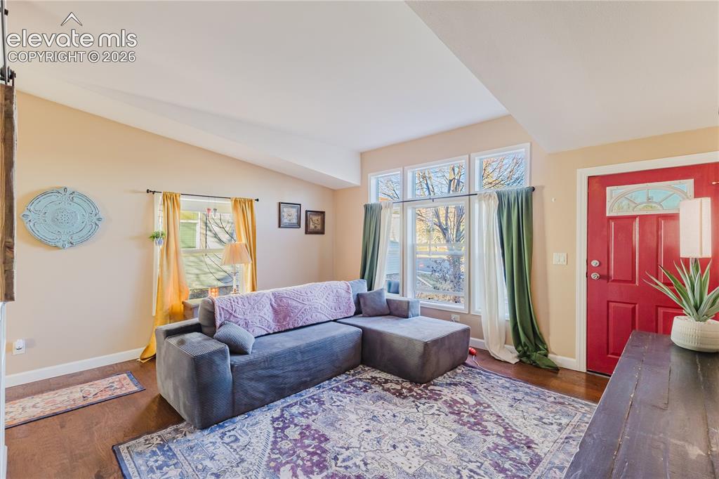 Image 8 of 30: Living area featuring vaulted ceilings, wood-finish flooring, a vibrant red