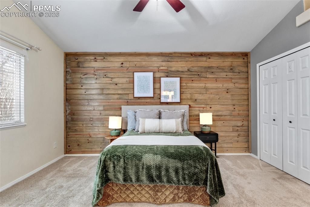Image 18 of 50: Carpeted bedroom with wooden walls, a closet, and a ceiling fan