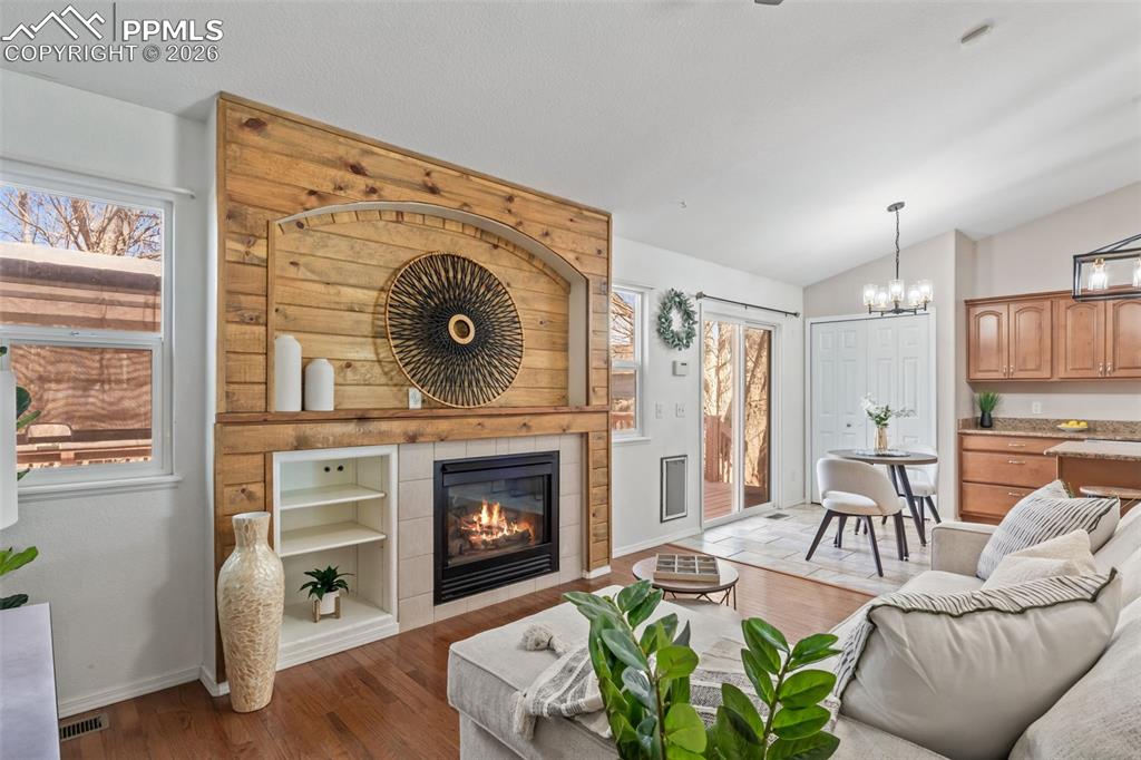 Image 9 of 50: Living area with dark wood-style floors, a tiled fireplace, vaulted ceiling