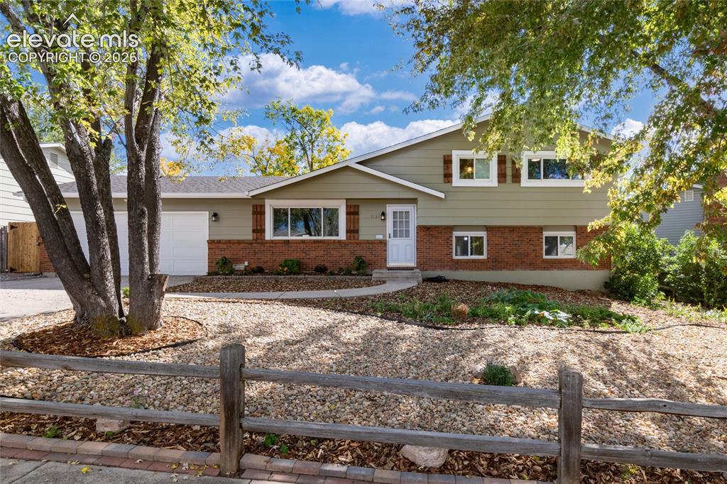 Caption: Split-level residence featuring brick and siding facade, a front-facing garage, and mature trees