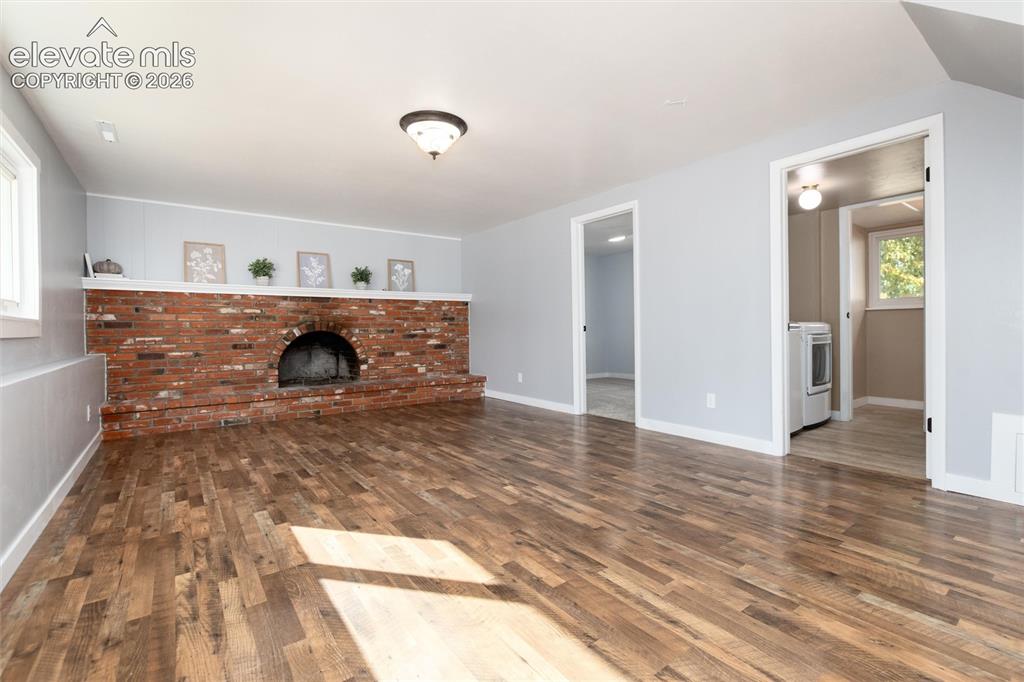 Image 23 of 47: Spacious room featuring wood-finish flooring, a brick fireplace with a whit