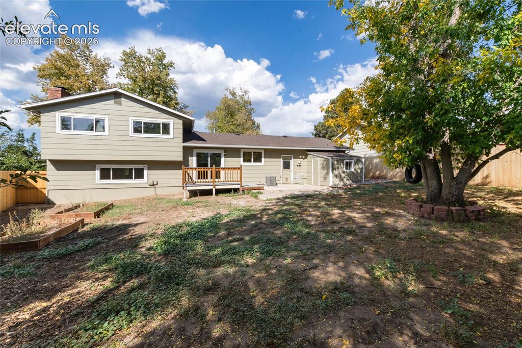Image 41 of 47: Expansive backyard with a wood privacy fence, a wood deck, and a mature tre