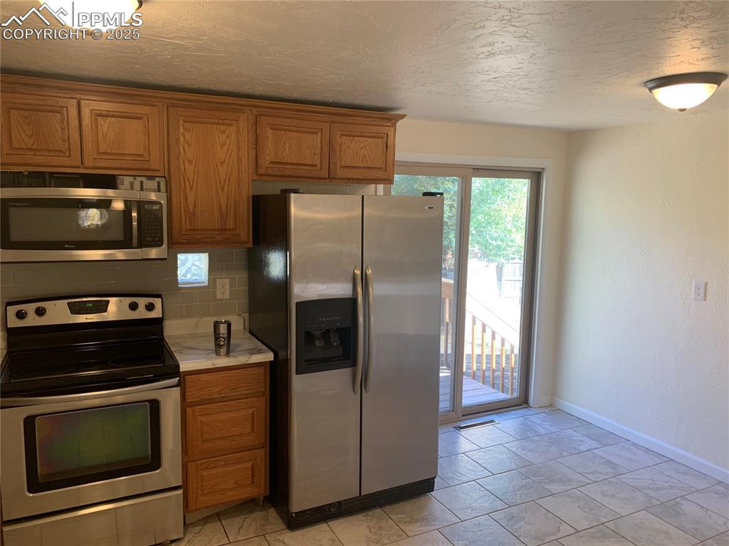 Image 3 of 32: Kitchen with stainless steel appliances, light countertops, brown cabinets,