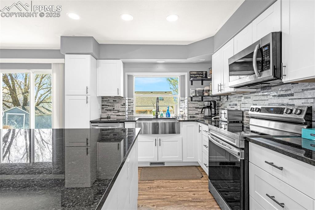 Image 2 of 17: Kitchen with white cabinetry, dark stone counters, a sink, light wood finis