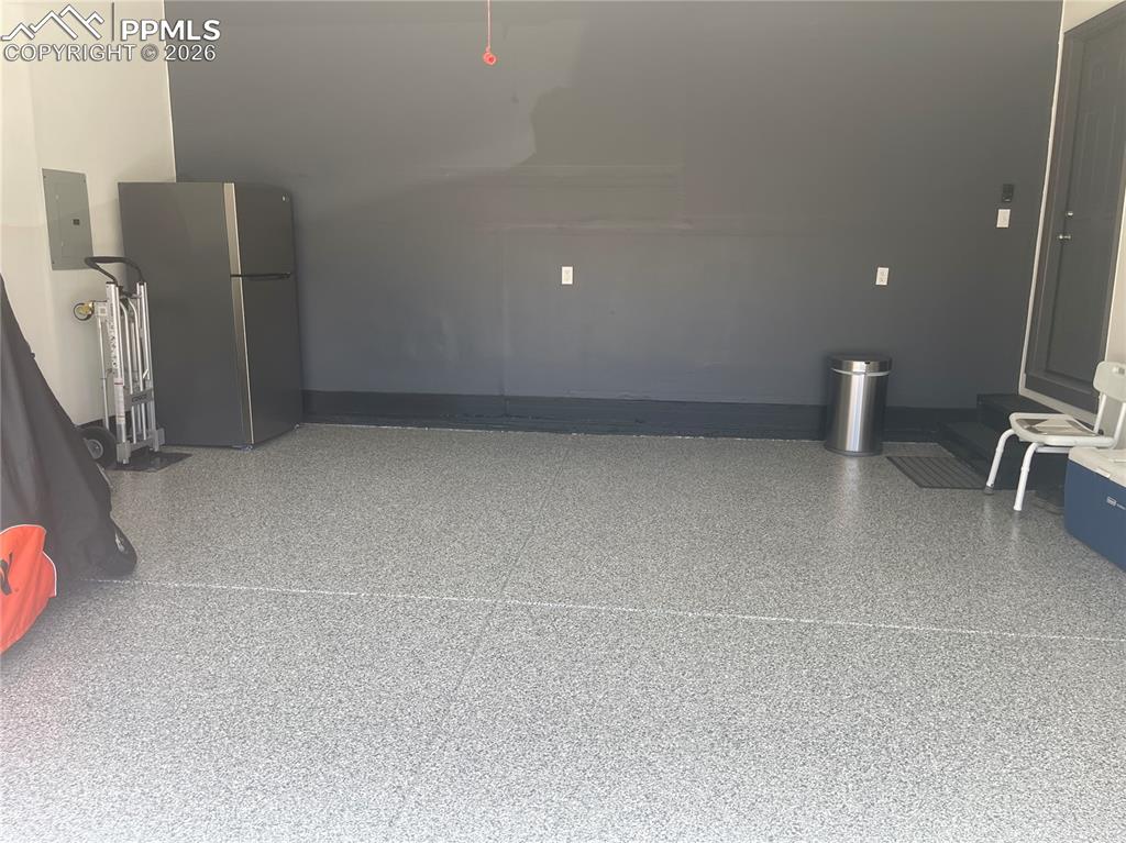 Image 17 of 19: Garage with freestanding refrigerator and electric panel