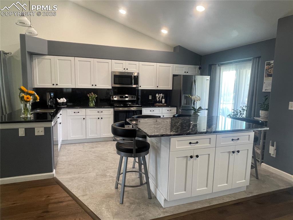 Image 4 of 19: Kitchen with a breakfast bar, vaulted ceiling, white cabinets, stainless st