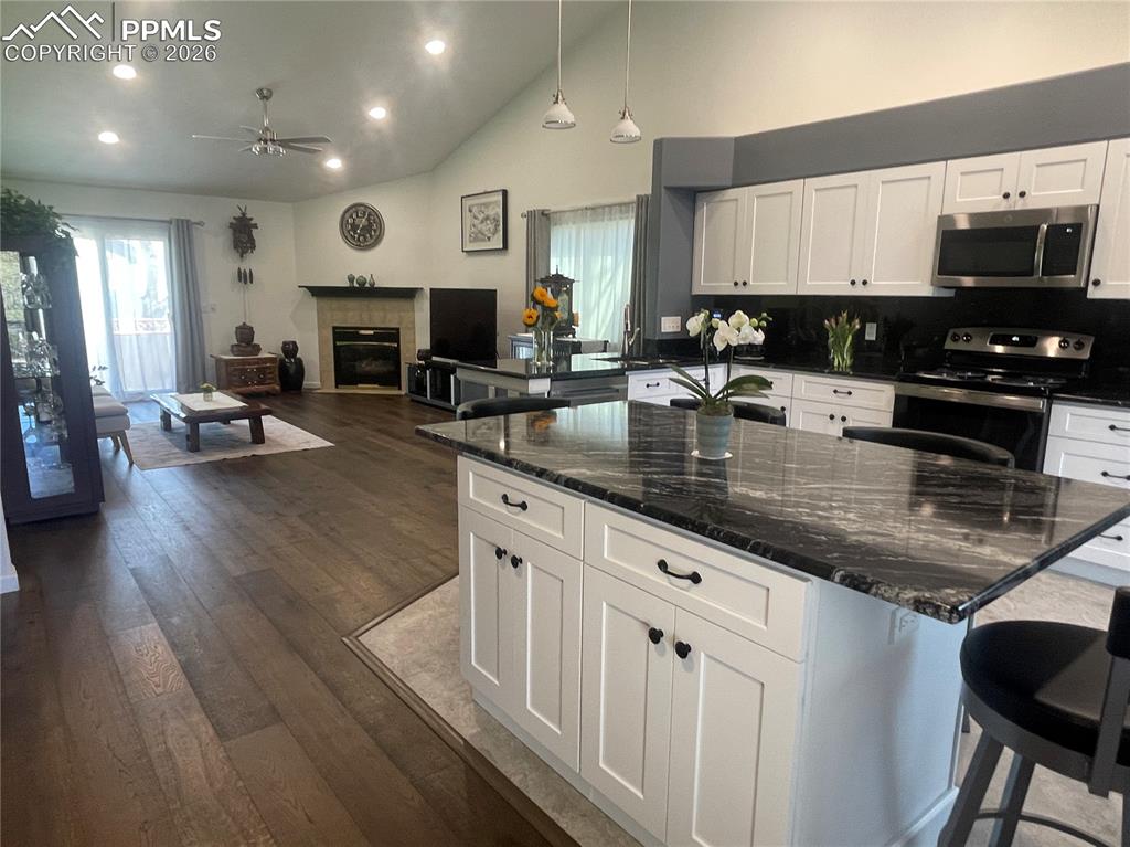 Image 5 of 19: Kitchen with a breakfast bar, white cabinetry, dark stone counters, dark wo