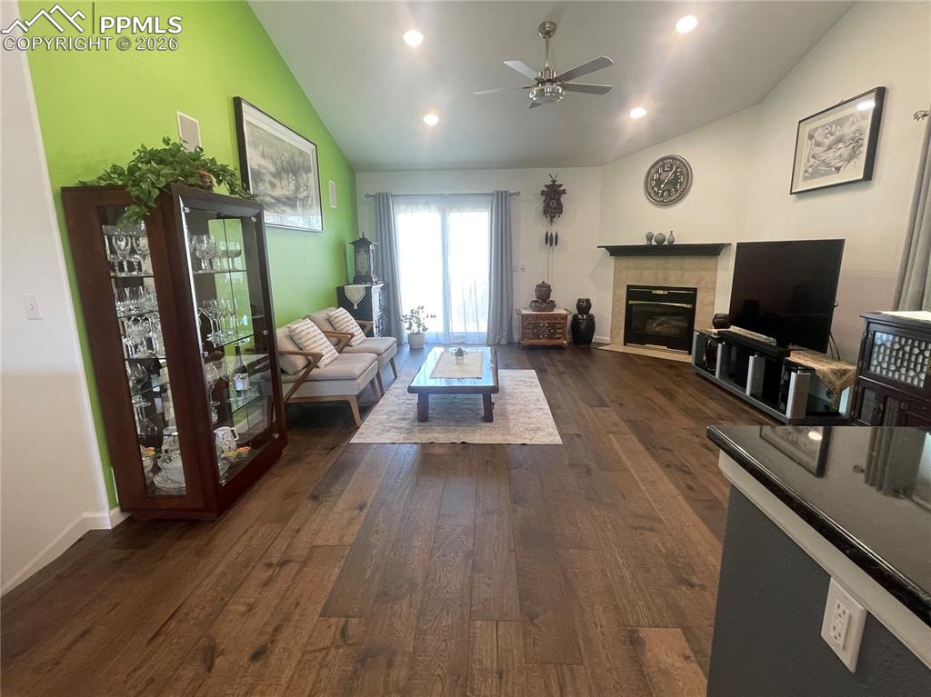Image 6 of 19: Living room with a fireplace, a ceiling fan, vaulted ceiling, dark wood-sty
