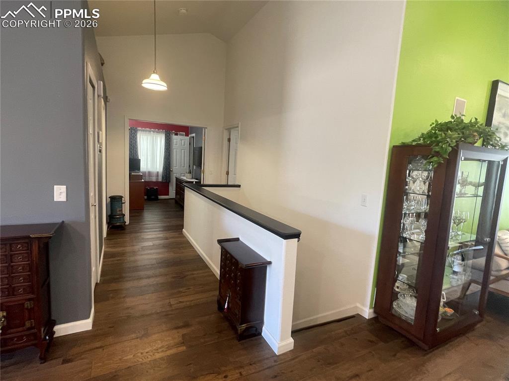 Image 7 of 19: Corridor with dark wood-style flooring, vaulted ceiling, and an upstairs la