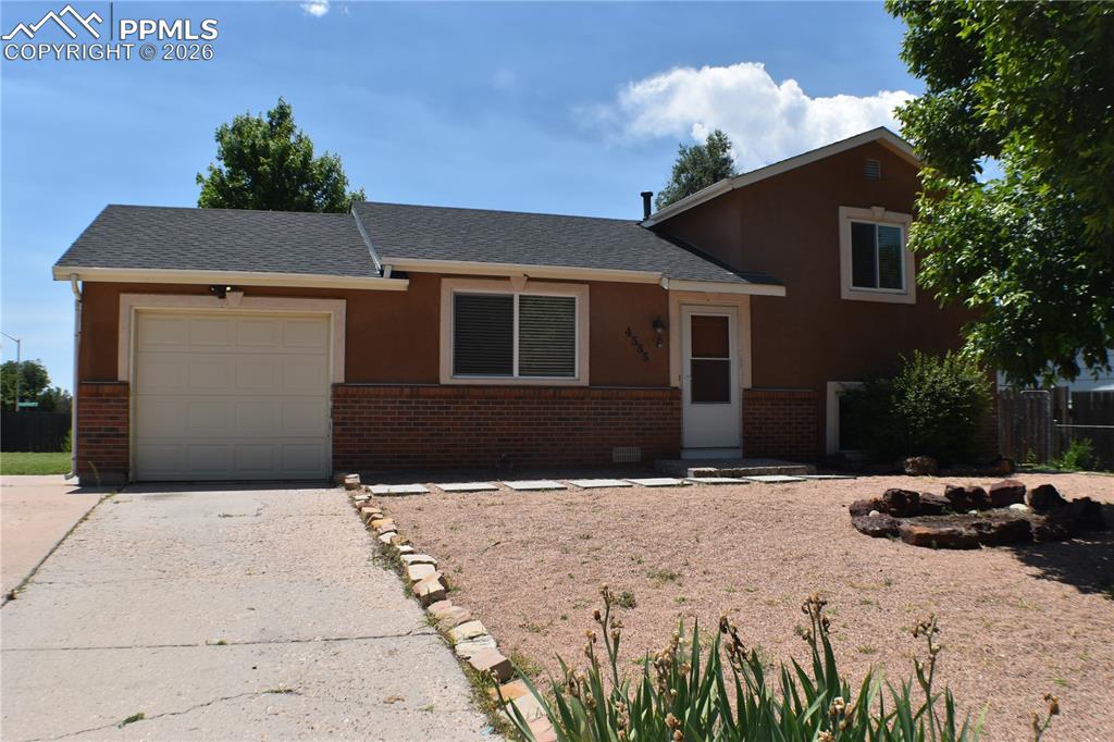 Caption: Tri-level home featuring brick siding, an attached garage, concrete driveway, and a shingled roof