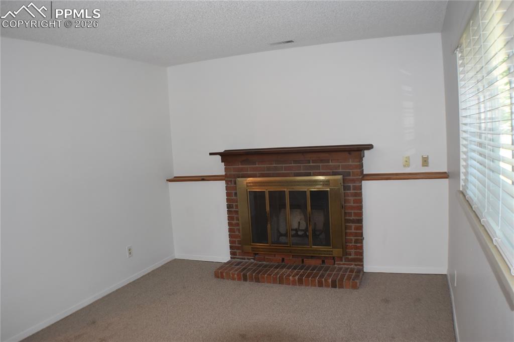 Image 18 of 40: Unfurnished living room featuring a brick fireplace, carpet, and a textured