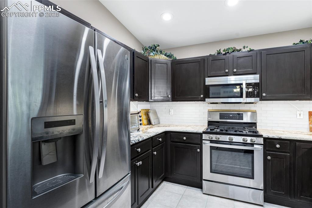 Image 10 of 44: Kitchen featuring stainless steel appliances, backsplash, light stone count